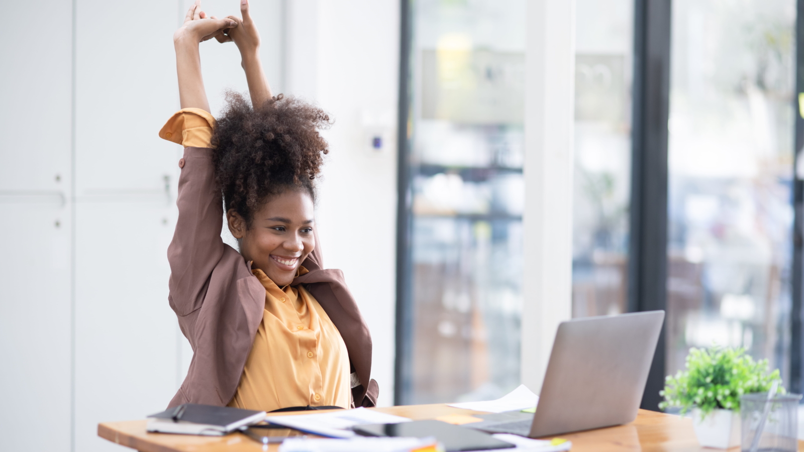 Office worker stretching arms overhead at her desk to relieve stress and support mental health during the workday