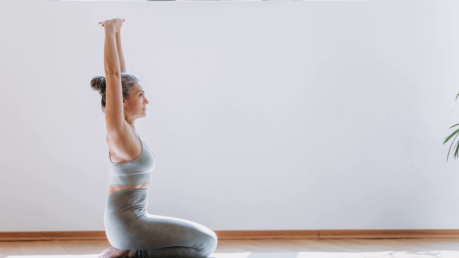 Woman seated on a yoga mat with arms raised, practicing mindful and controlled stretching