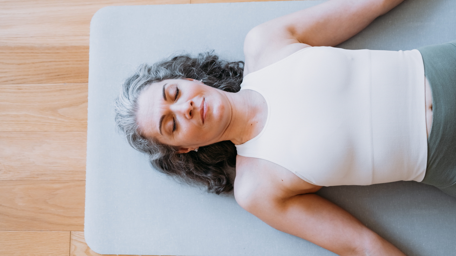 Woman lying on a yoga mat with eyes closed, resting and focusing on relaxation and recovery