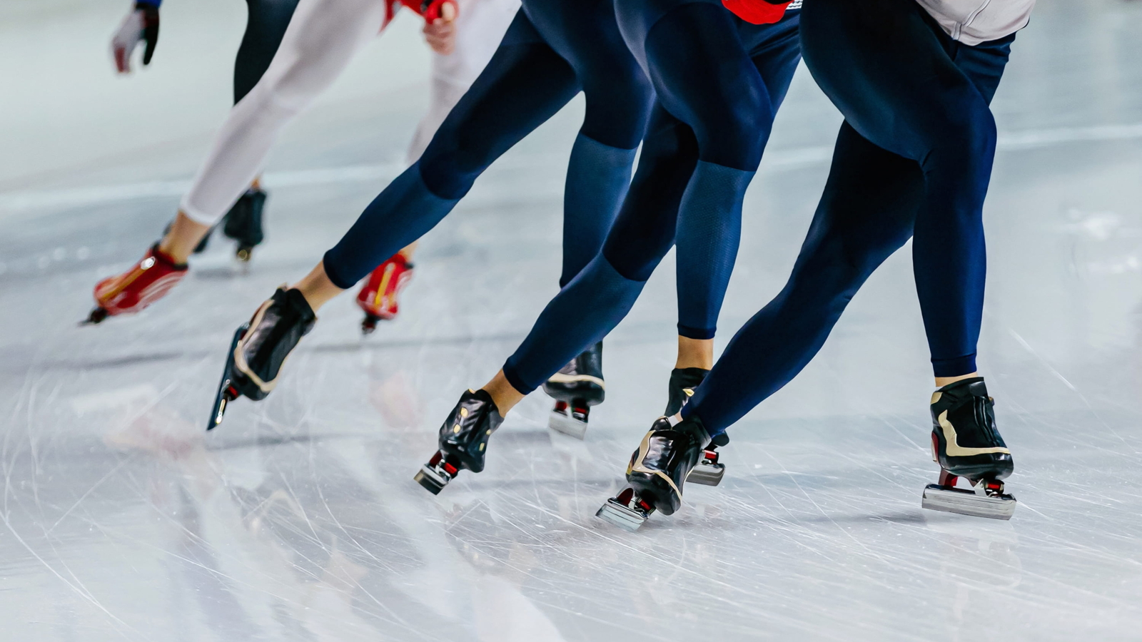 Speed skaters racing on an ice track during a competition, demonstrating powerful stride mechanics and lower body engagement