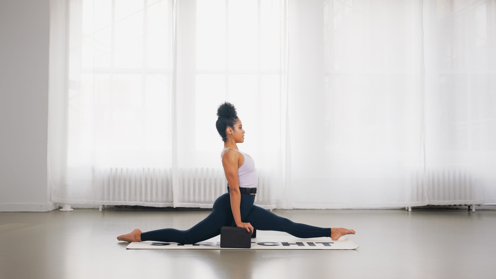 Front split variation with yoga block under hands demonstrating active resistance engagement and strength in long-range hip extension.
