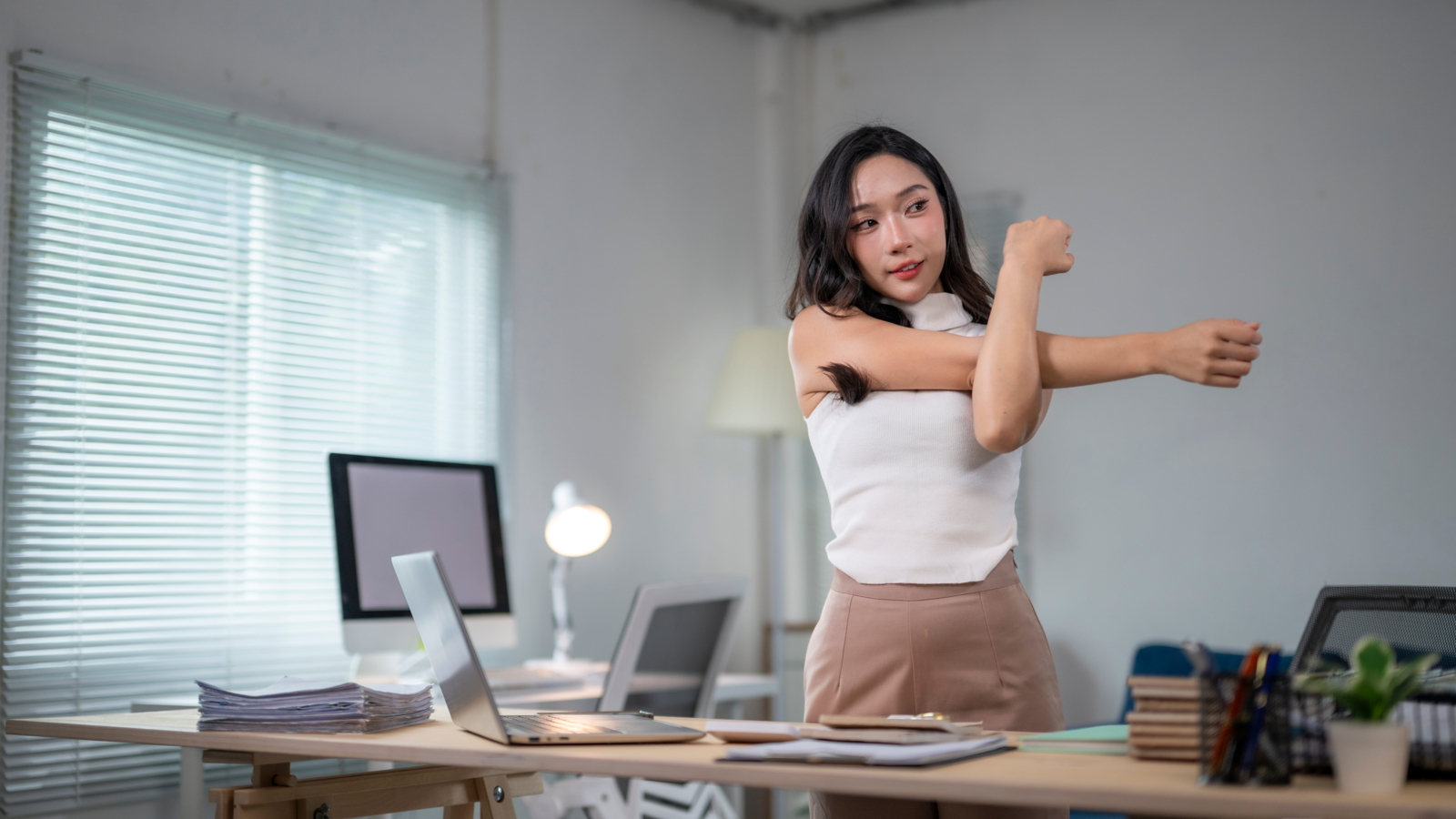 young woman stretching her upper body at a desk during a short movement break to relieve tension from sitting