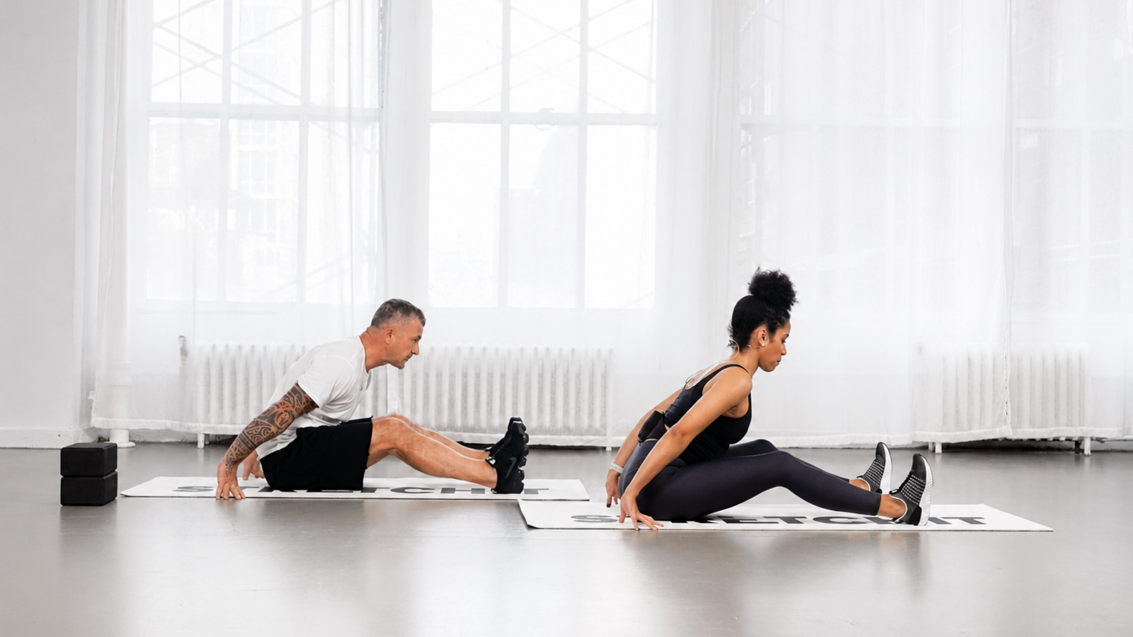 STRETCHIT trainer Alicia Archer and a participant demonstrating a seated pike stretch with bent knees STRETCHIT trainer Alicia Archer and a participant demonstrating a seated pike stretch with bent knees